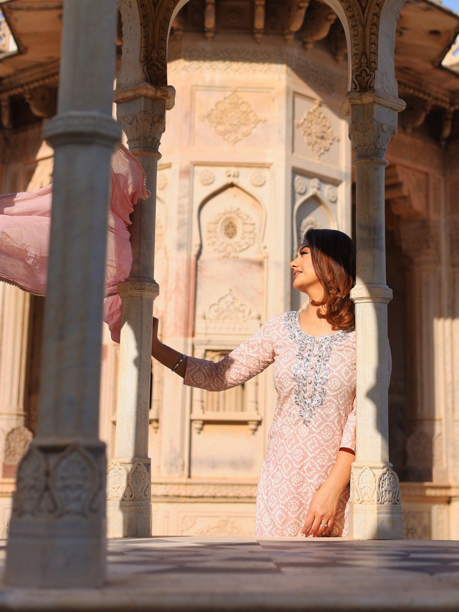 Woman in a white lace dress poses beside an ornate structure, showcasing a kurta palazzo set