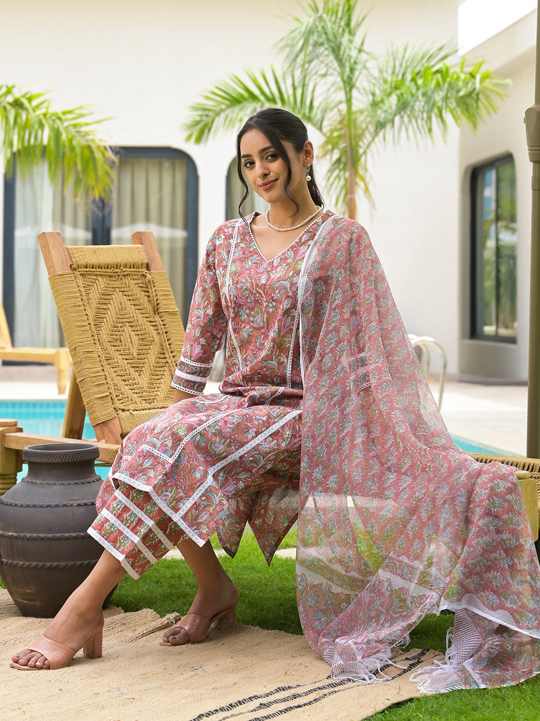 Woman in a pink floral traditional outfit on a wicker chair, showcasing Maroon Floral Print Cotton Handblock Kurta Set for Women