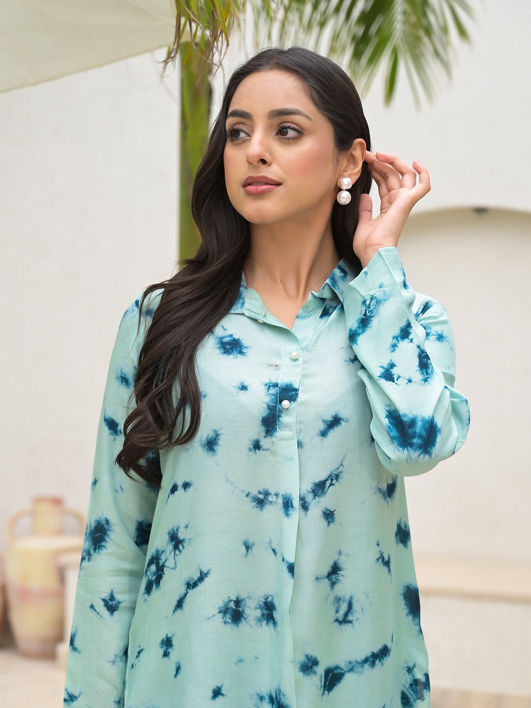 Woman wearing a light blue tie-dye patterned shirt with long sleeves.